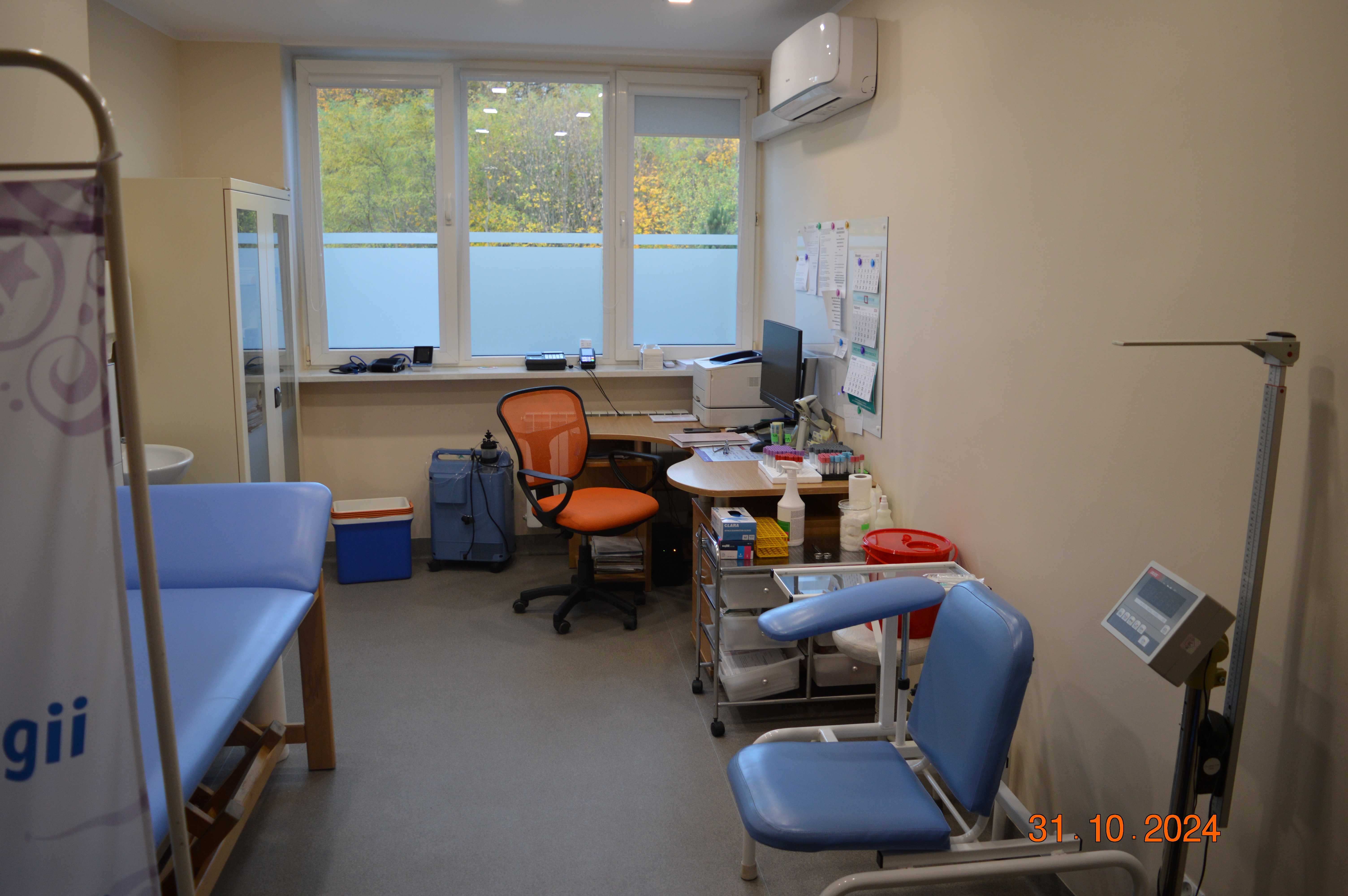 Wnętrze pracowni EKG w części centralnej widoczne biurko z przyrządem obok innego parawan za którym stoi leżanka.